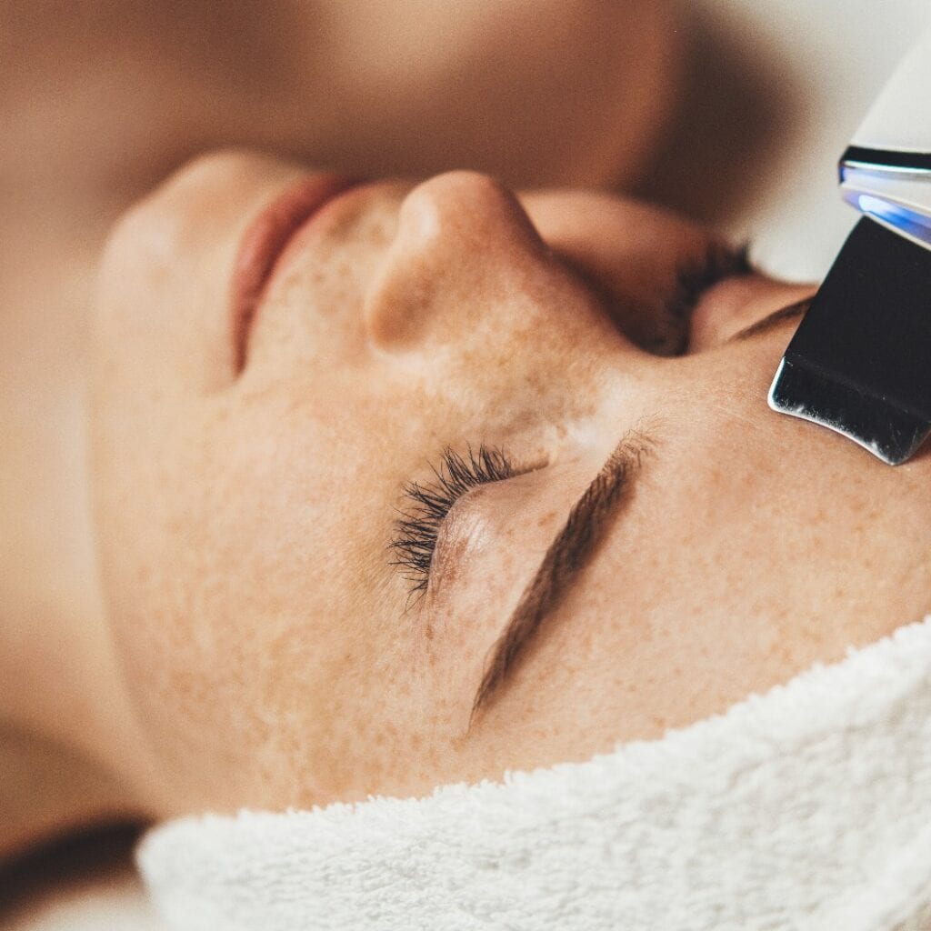 Caucasian freckled woman receiving face cavitation procedure at spa salon. Professional peeling hardware. Electric spa equipment. Medicine patient device
