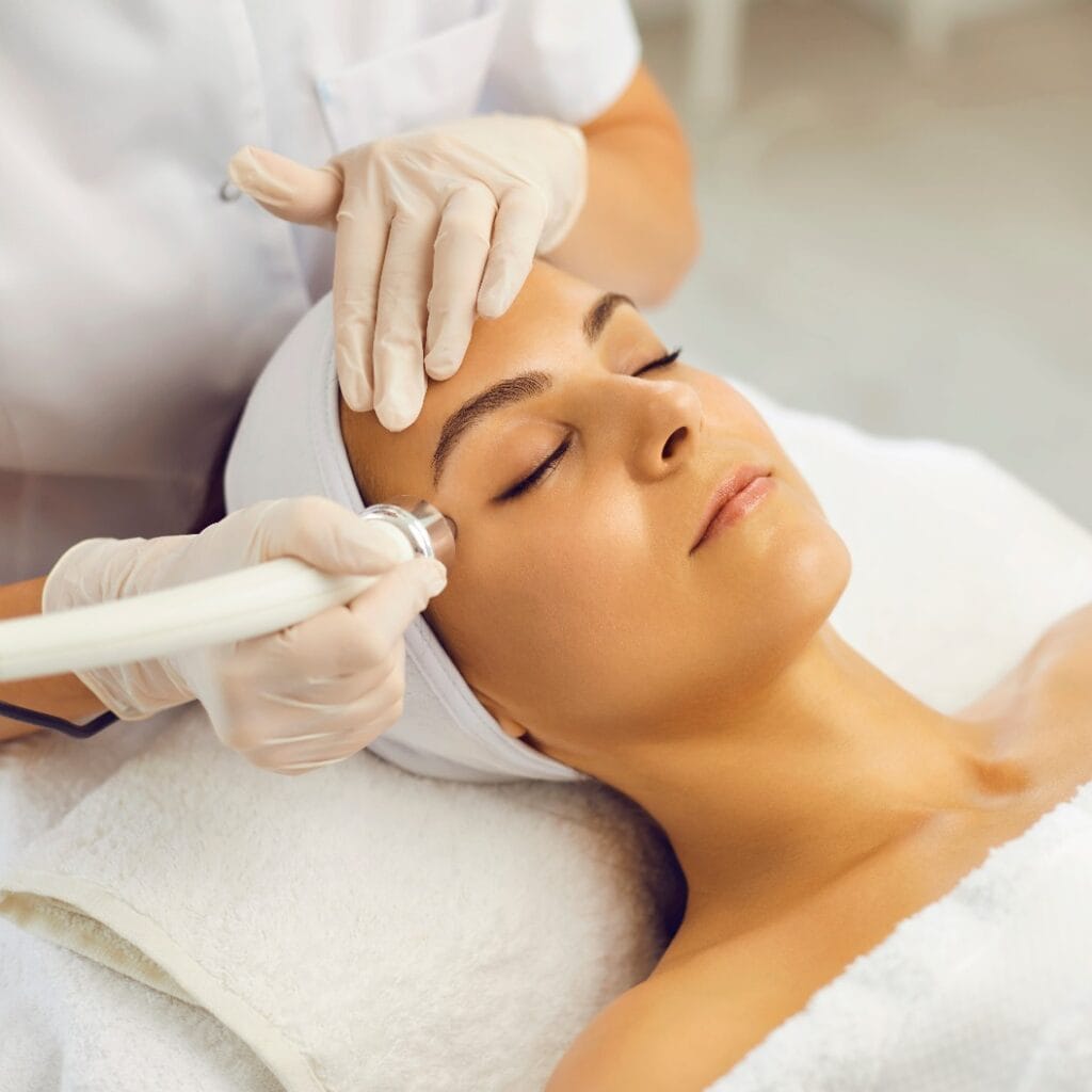 Cosmetologist making vacuum facial skin cleaning for young woman in beauty salon